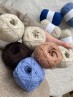 Hand holding several Ruke Wool yarn balls in different natural shades including blue, beige, and brown Hand holding several Ruke Wool yarn balls in different natural shades including blue, beige, and brown