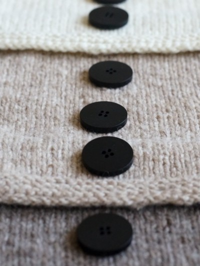Close-up of Ruke black 28 mm four-hole bioresin buttons on beige knit
