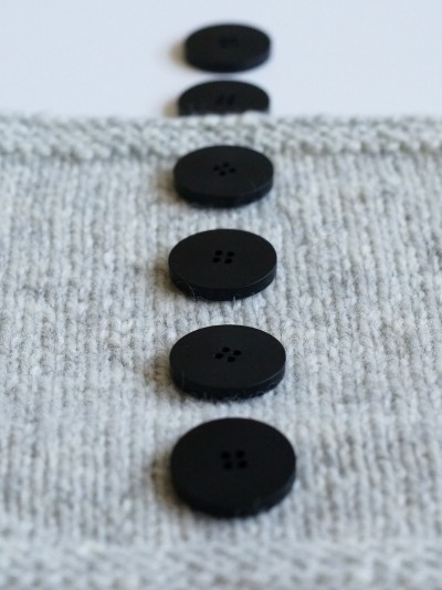Side view of Ruke black 28 mm four-hole bioresin buttons on light grey knit