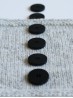 Side view of Ruke black 28 mm four-hole bioresin buttons on light grey knit