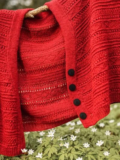 Red Ruke Moon cardigan knitting pattern hanging outdoors with black buttons and flower meadow