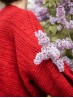 Back detail of the red Ruke Moon cardigan knitting pattern beside lilac flowers