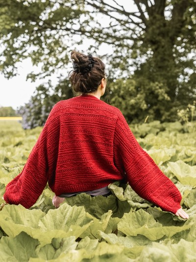 Oversized back fit of the red Ruke Moon cardigan knitting pattern in a green meadow