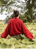 Oversized back fit of the red Ruke Moon cardigan knitting pattern in a green meadow
