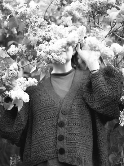 Black and white portrait of a model wearing the Ruke Moon cardigan knitting pattern among lilacs
